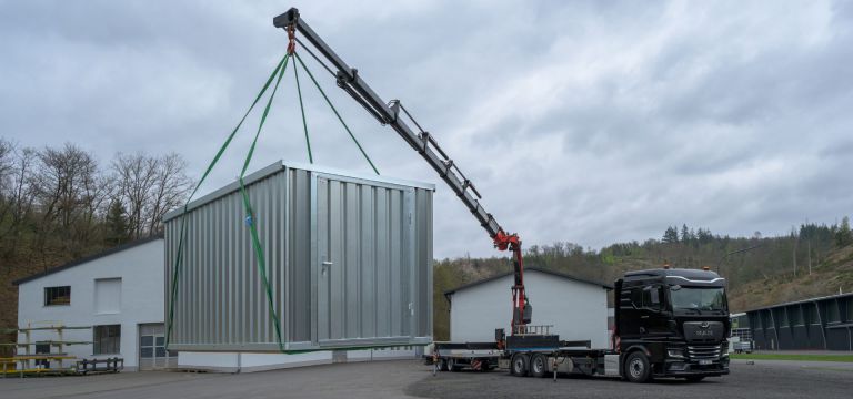 Ein Kran mit einen montierten FLADAFI Lagercontainer auf die Ladefläche eines LKW